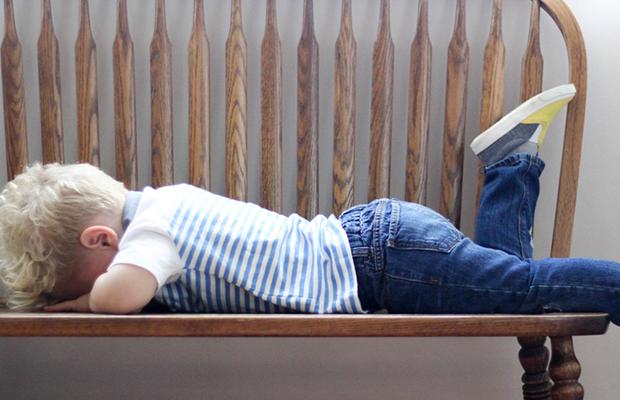 little boy laying face down in time-out on a wood bench